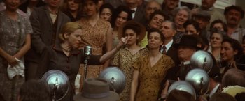 Movie still from “Evita” (1996), directed by Alan Parker – An old fashioned microphone in front of a crowd of people; Medium shot, Over the shoulder angle