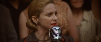 Movie still from “Evita” (1996), directed by Alan Parker – A person holding a microphone; Close Up shot, Over the shoulder angle