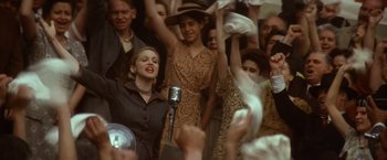 Movie still from “Evita” (1996), directed by Alan Parker – A group of people standing in a crowd with a microphone; Medium shot, Low angle