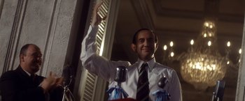 Movie still from “Evita” (1996), directed by Alan Parker – A man in a white dress shirt and tie holding a microphone; Close Up shot, Low angle