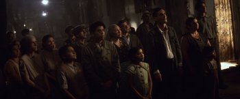 Movie still from “Evita” (1996), directed by Alan Parker – A group of people standing in a dark room; Medium shot, Low angle