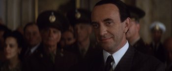 Movie still from “Evita” (1996), directed by Alan Parker – A man in a suit and tie in front of a group of men; Close Up shot, Low angle