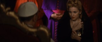 Movie still from “Evita” (1996), directed by Alan Parker – A woman in a black dress is standing next to a man in a purple suit; Close Up shot, Over the shoulder angle