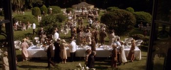 Movie still from “Evita” (1996), directed by Alan Parker – A group of people standing around a table with food on top of it; Extreme Wide shot, High angle