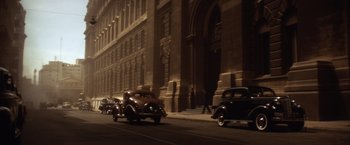 Movie still from “Evita” (1996), directed by Alan Parker – An old car driving down a street past a tall building at night; Extreme Wide shot, High angle