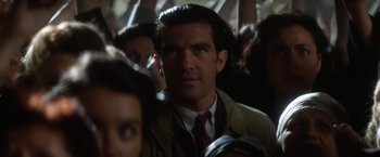 Movie still from “Evita” (1996), directed by Alan Parker – A person wearing a suit and tie; Close Up shot, Over the shoulder angle