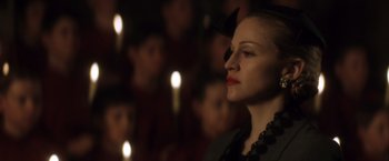 Movie still from “Evita” (1996), directed by Alan Parker – A woman with a bow in front of a group of candles; Close Up shot, Over the shoulder angle