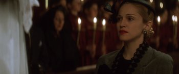 Movie still from “Evita” (1996), directed by Alan Parker – A woman with a bow in her hair is in front of a group of candles; Close Up shot, Over the shoulder angle