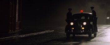 Movie still from “Evita” (1996), directed by Alan Parker – A man standing in front of a car at night; Wide shot, Low angle
