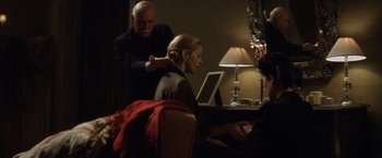 Movie still from “Evita” (1996), directed by Alan Parker – A woman sitting in front of a computer while a man stands next to her; Medium shot, Over the shoulder angle