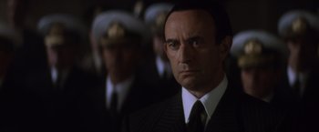 Movie still from “Evita” (1996), directed by Alan Parker – A man in a suit and tie in front of a group of people; Close Up shot, Low angle