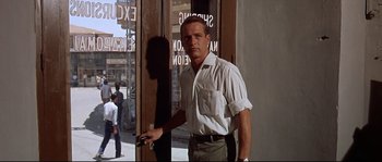 Movie still from “Exodus” (1960), directed by Otto Preminger – A man standing in front of a building holding a cell phone; Medium shot, Low angle