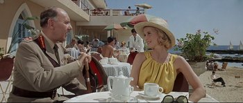 Movie still from “Exodus” (1960), directed by Otto Preminger – A woman wearing a hat sitting at an outdoor table; Medium shot, Low angle