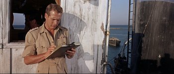 Movie still from “Exodus” (1960), directed by Otto Preminger – A man standing next to the ocean writing on a clipboard; Medium shot, Over the shoulder angle