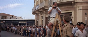 Movie still from “Exodus” (1960), directed by Otto Preminger – A man standing on top of a ladder while holding a camera; Wide shot, Low angle