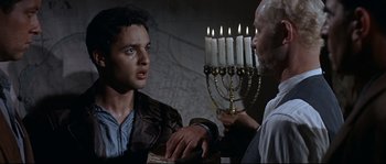 Movie still from “Exodus” (1960), directed by Otto Preminger – A man is talking to another man in front of a menorah; Medium shot, Over the shoulder angle