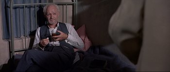 Movie still from “Exodus” (1960), directed by Otto Preminger – An older man sitting on a bed holding a glass of beer; Medium shot, High angle