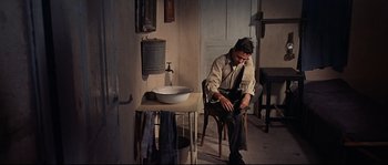 Movie still from “Exodus” (1960), directed by Otto Preminger – A man sitting on a chair in a room with a sink; Wide shot, High angle