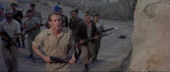 Movie still from “Exodus” (1960), directed by Otto Preminger – A group of men walking down a dirt road holding guns; Medium shot, Low angle