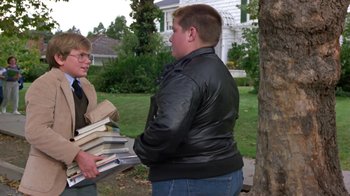 Movie still from “Explorers” (1985), directed by Joe Dante – A man in a leather jacket holding a stack of books; Medium shot, Low angle