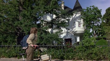 Movie still from “Explorers” (1985), directed by Joe Dante – A woman walking down the street in front of a white house; Wide shot, Low angle