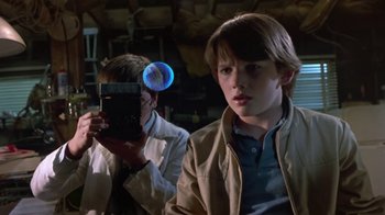 Movie still from “Explorers” (1985), directed by Joe Dante – A boy is holding a camera in a room; Close Up shot, Over the shoulder angle
