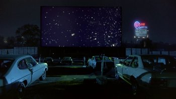 Movie still from “Explorers” (1985), directed by Joe Dante – Cars are parked in front of a large screen at a drive - in theater; Extreme Wide shot, Low angle