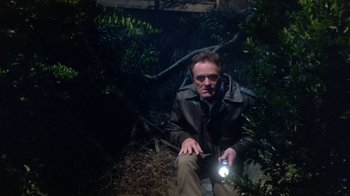 Movie still from “Explorers” (1985), directed by Joe Dante – A man sitting in the middle of a forest at night with a flashlight; Medium shot, Low angle