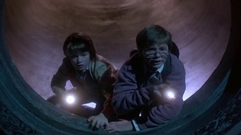 Movie still from “Explorers” (1985), directed by Joe Dante – A couple of people that are standing up in a tunnel; Medium shot, Overhead angle