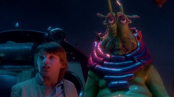 Movie still from “Explorers” (1985), directed by Joe Dante – A man standing next to an alien in a dark room; Medium shot, Low angle