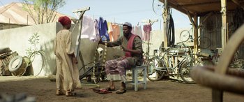 Movie still from “Eye in the Sky” (2015), directed by Gavin Hood – A man sitting on top of a wooden bench; Wide shot, Low angle