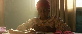 Movie still from “Eye in the Sky” (2015), directed by Gavin Hood – A woman sitting at a table writing on a piece of paper; Medium shot, Over the shoulder angle