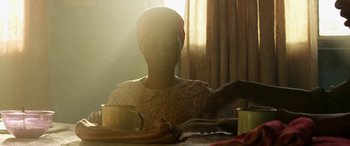 Movie still from “Eye in the Sky” (2015), directed by Gavin Hood – A woman sitting at a table with a cup of coffee; Medium shot, Low angle
