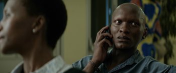 Movie still from “Eye in the Sky” (2015), directed by Gavin Hood – A man talking on a cell phone in front of another man; Close Up shot, Over the shoulder angle