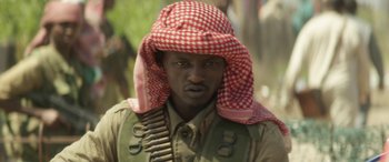 Movie still from “Eye in the Sky” (2015), directed by Gavin Hood – A man with a red and white headscarf on; Close Up shot, Over the shoulder angle