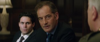 Movie still from “Eye in the Sky” (2015), directed by Gavin Hood – A person wearing a suit and tie; Close Up shot, Over the shoulder angle