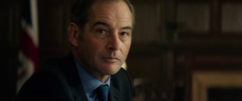 Movie still from “Eye in the Sky” (2015), directed by Gavin Hood – A person wearing a suit and tie; Close Up shot, Over the shoulder angle