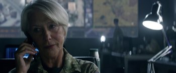 Movie still from “Eye in the Sky” (2015), directed by Gavin Hood – An older woman in a military uniform sitting in a chair; Close Up shot, Over the shoulder angle