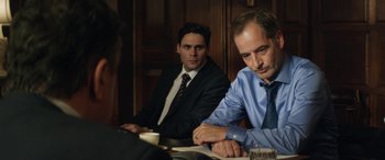 Movie still from “Eye in the Sky” (2015), directed by Gavin Hood – A couple of men sitting at a wooden table; Medium shot, Over the shoulder angle