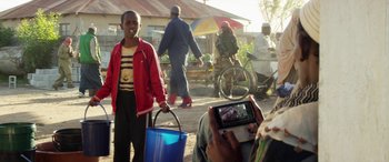 Movie still from “Eye in the Sky” (2015), directed by Gavin Hood – A man taking a picture of a woman holding a blue bucket; Medium shot, Over the shoulder angle
