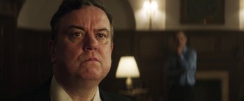 Movie still from “Eye in the Sky” (2015), directed by Gavin Hood – A person wearing a suit and tie; Close Up shot, Low angle