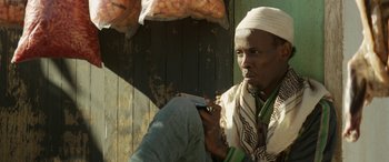 Movie still from “Eye in the Sky” (2015), directed by Gavin Hood – A man sitting on the ground holding a cell phone to his ear; Close Up shot, Low angle