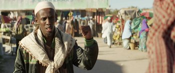 Movie still from “Eye in the Sky” (2015), directed by Gavin Hood – A man in a crowd of people on a street; Medium shot, Over the shoulder angle