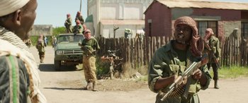 Movie still from “Eye in the Sky” (2015), directed by Gavin Hood – A group of men standing next to each other on a dirt road; Medium shot, Low angle