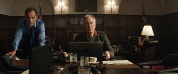 Movie still from “Eye in the Sky” (2015), directed by Gavin Hood – A man in a military uniform sitting in front of a computer; Medium shot, Low angle