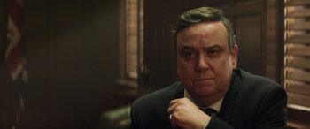 Movie still from “Eye in the Sky” (2015), directed by Gavin Hood – A person wearing a suit and tie; Close Up shot, Over the shoulder angle