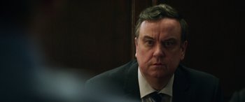 Movie still from “Eye in the Sky” (2015), directed by Gavin Hood – A person wearing a suit and tie; Close Up shot, Over the shoulder angle
