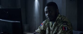 Movie still from “Eye in the Sky” (2015), directed by Gavin Hood – A man in a military uniform sitting in a room; Close Up shot, Over the shoulder angle
