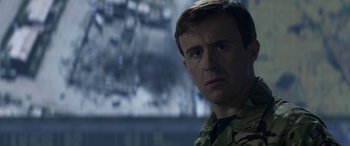 Movie still from “Eye in the Sky” (2015), directed by Gavin Hood – A man in military fatigues is looking at the camera; Close Up shot, Over the shoulder angle