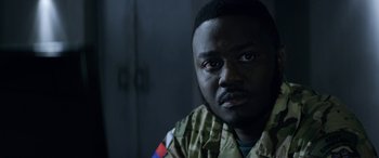 Movie still from “Eye in the Sky” (2015), directed by Gavin Hood – A man in a military uniform stares into the camera; Close Up shot, Over the shoulder angle